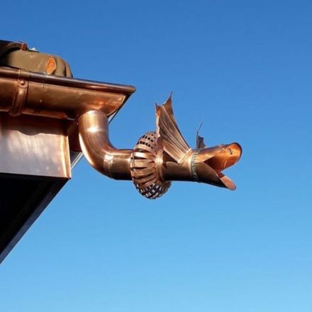 Descente en cuivre en forme de dragon sur un toit, contre un ciel bleu clair.