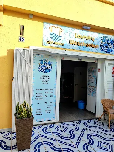 Fachada de tienda de servicio de lavandería con detalles en azul y blanco, planta en maceta y entrada de azulejos.