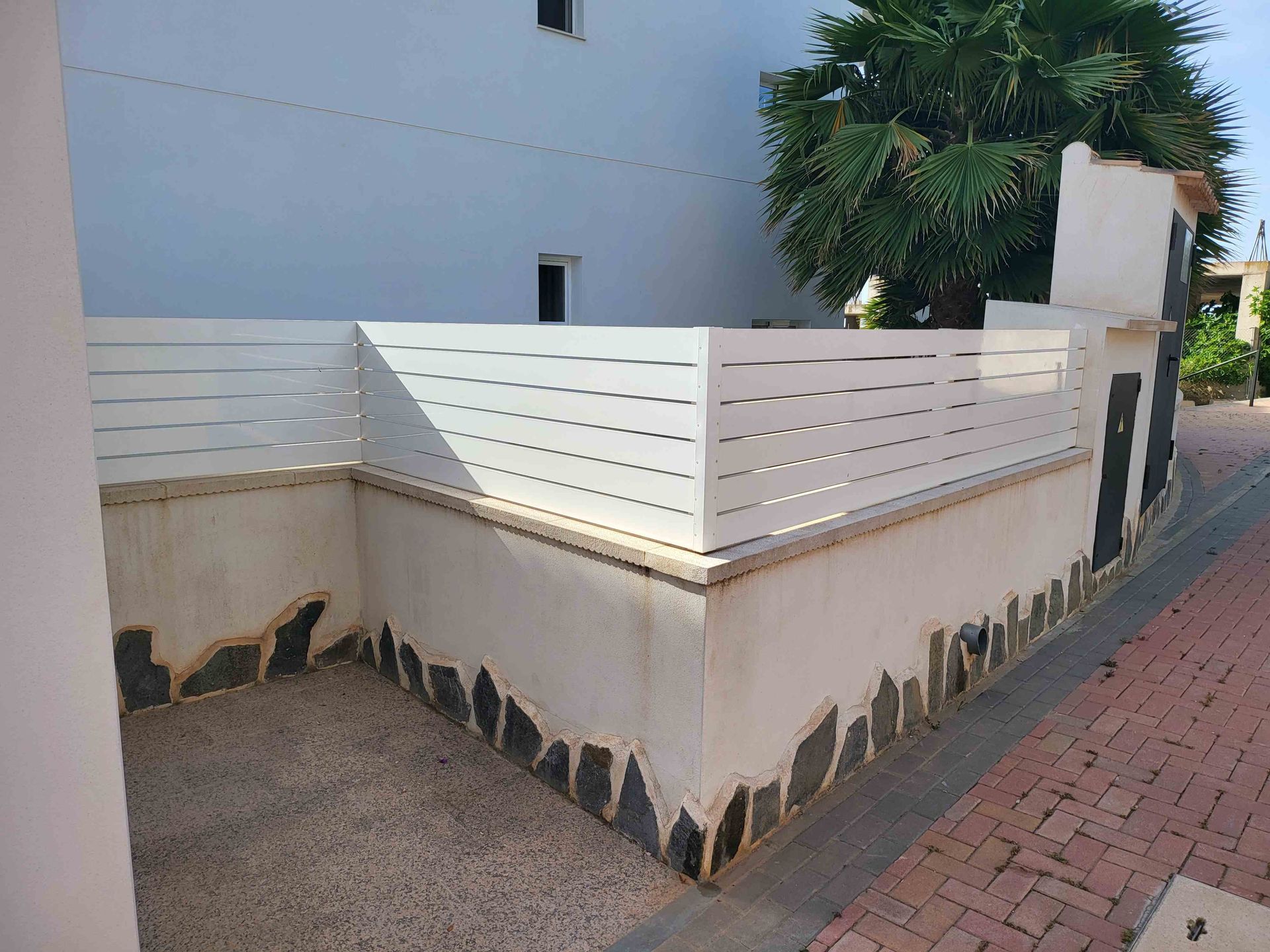 Una valla blanca está situada al costado de una pared de ladrillos.