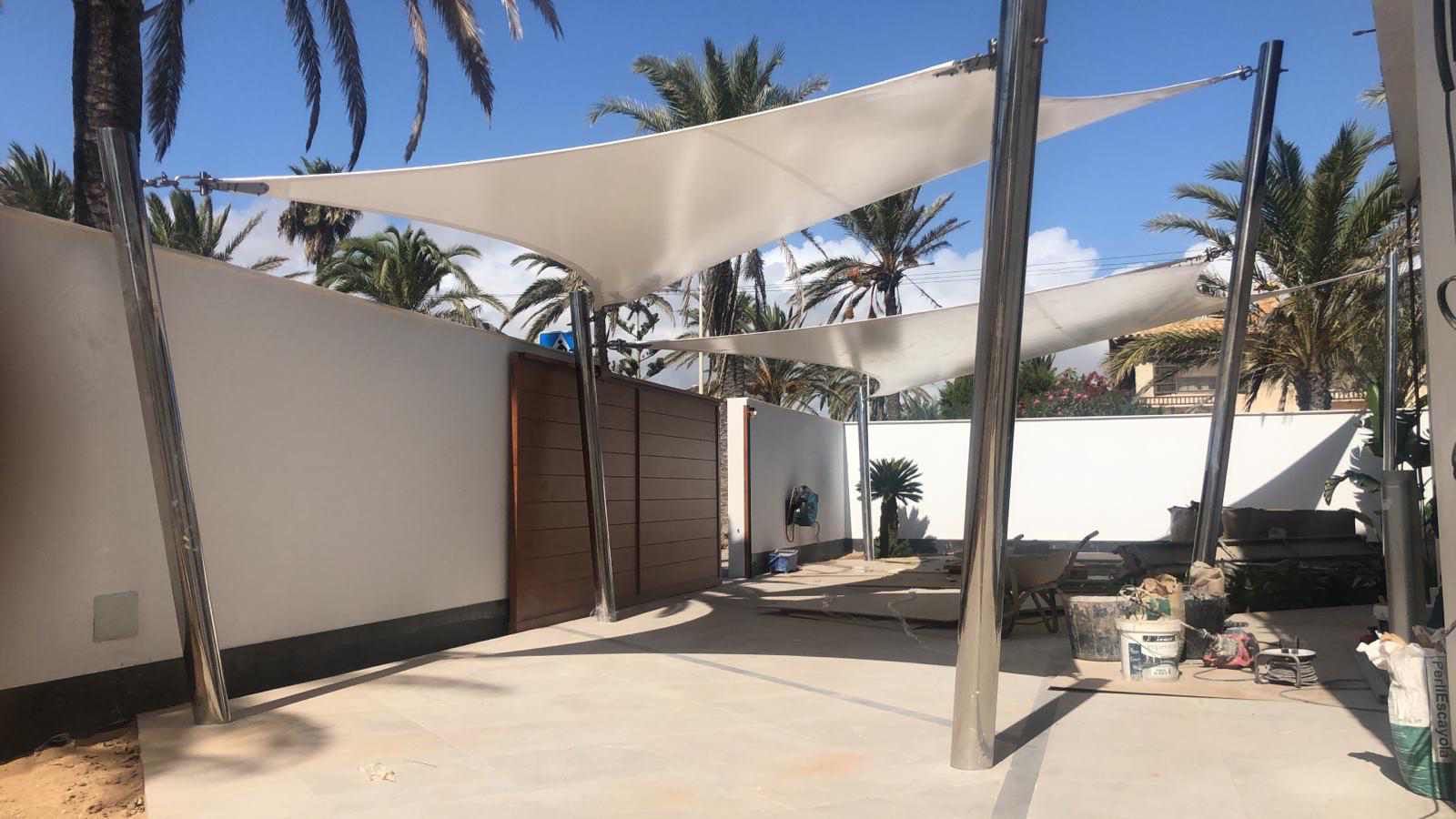 Un patio con una sombrilla blanca y palmeras al fondo.