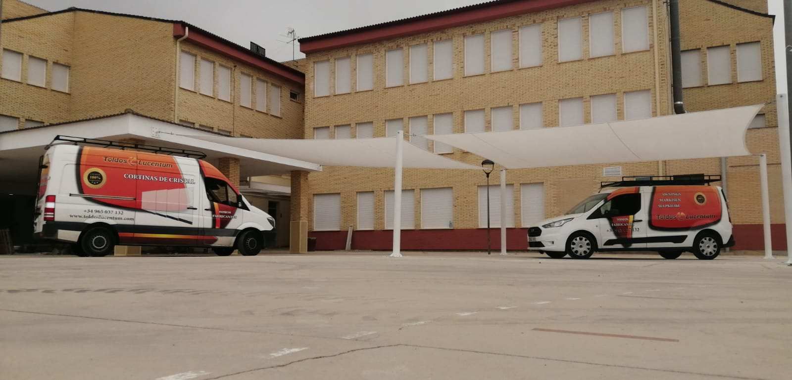 Dos furgonetas están estacionadas frente a un edificio bajo una marquesina.