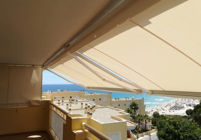 Un balcón con toldo con vista al mar y a los edificios.