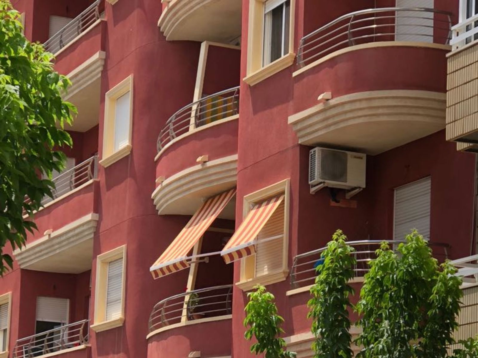 Un edificio rojo con muchos balcones y toldos.
