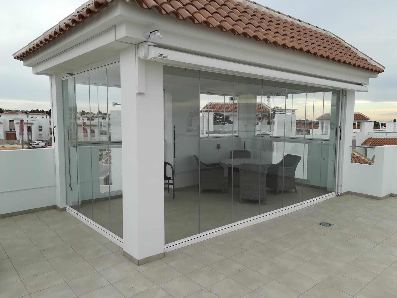 Un patio con mesa y sillas bajo un techo de cristal.