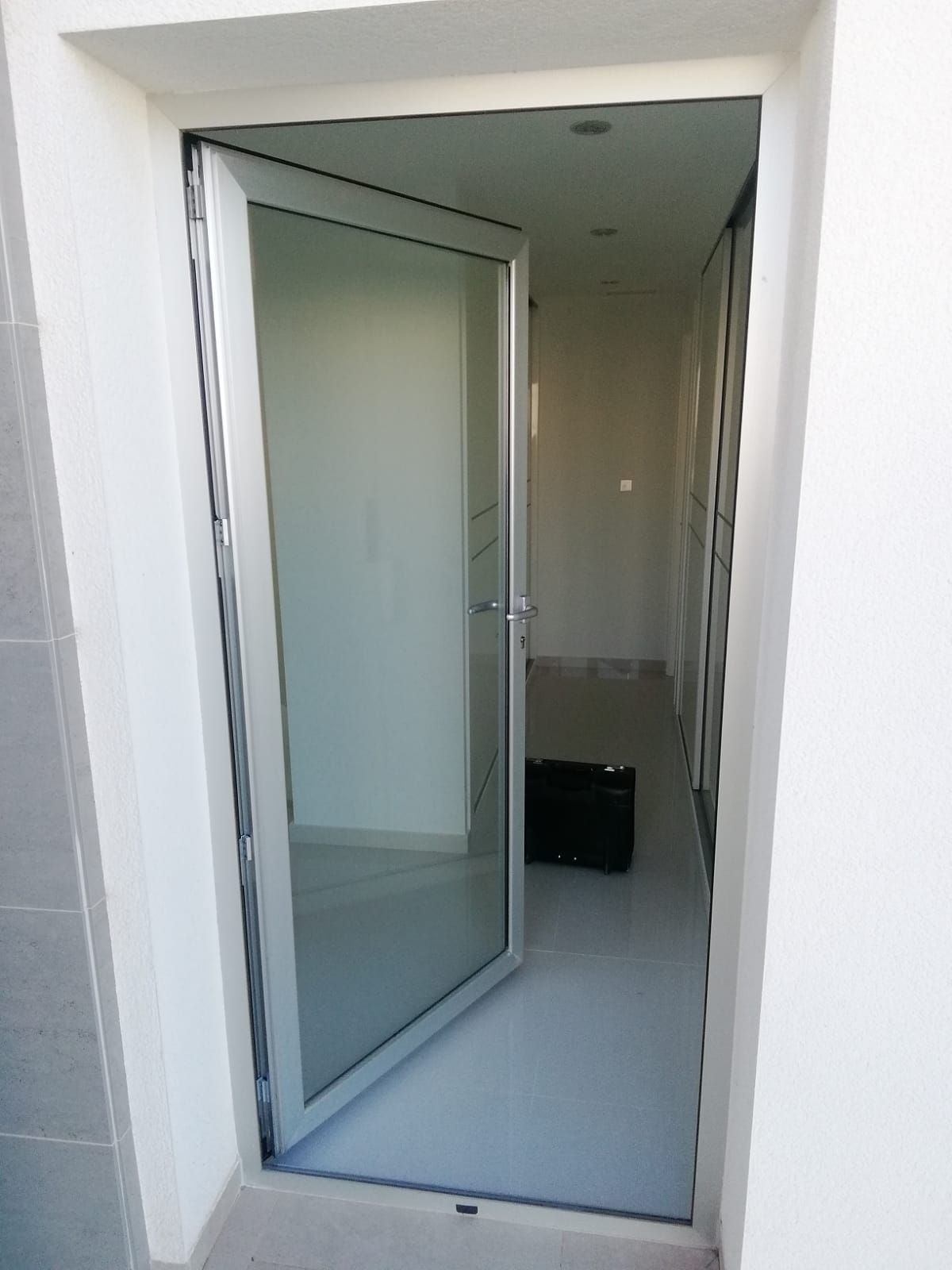 Una puerta de vidrio está abierta a un pasillo con una bolsa negra en el suelo.