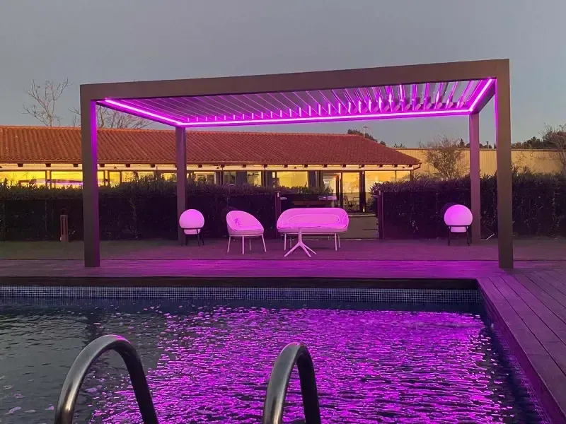 Una piscina con luces violetas y una pérgola sobre ella.