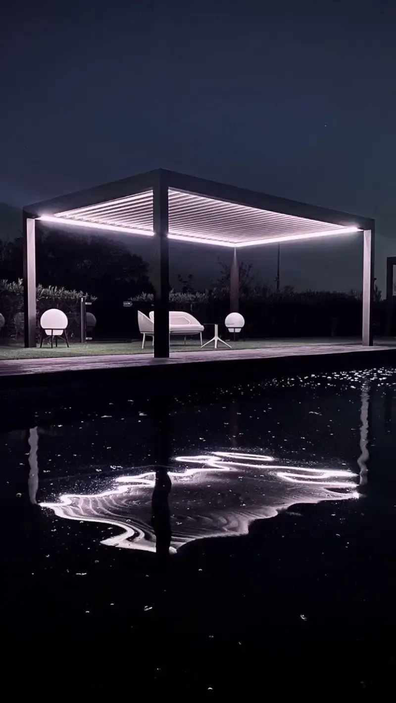 Una pérgola se ilumina por la noche junto a una piscina.