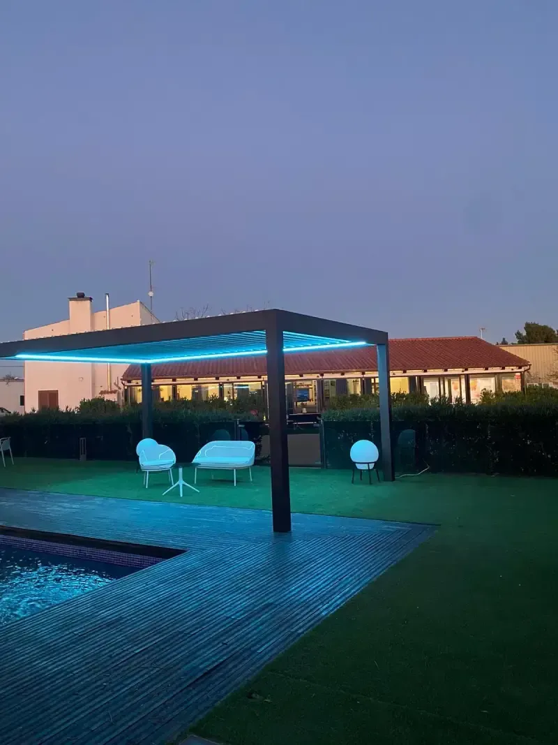 Una pérgola se ilumina por la noche frente a una piscina.