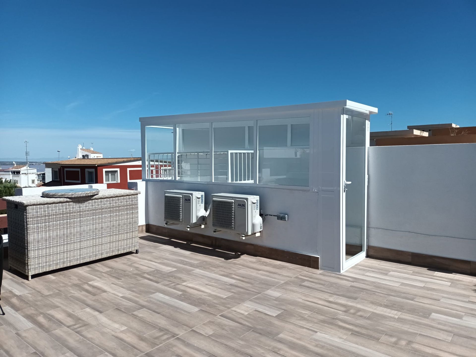 Una terraza en la azotea con un sofá de mimbre y algunos aparatos de aire acondicionado.