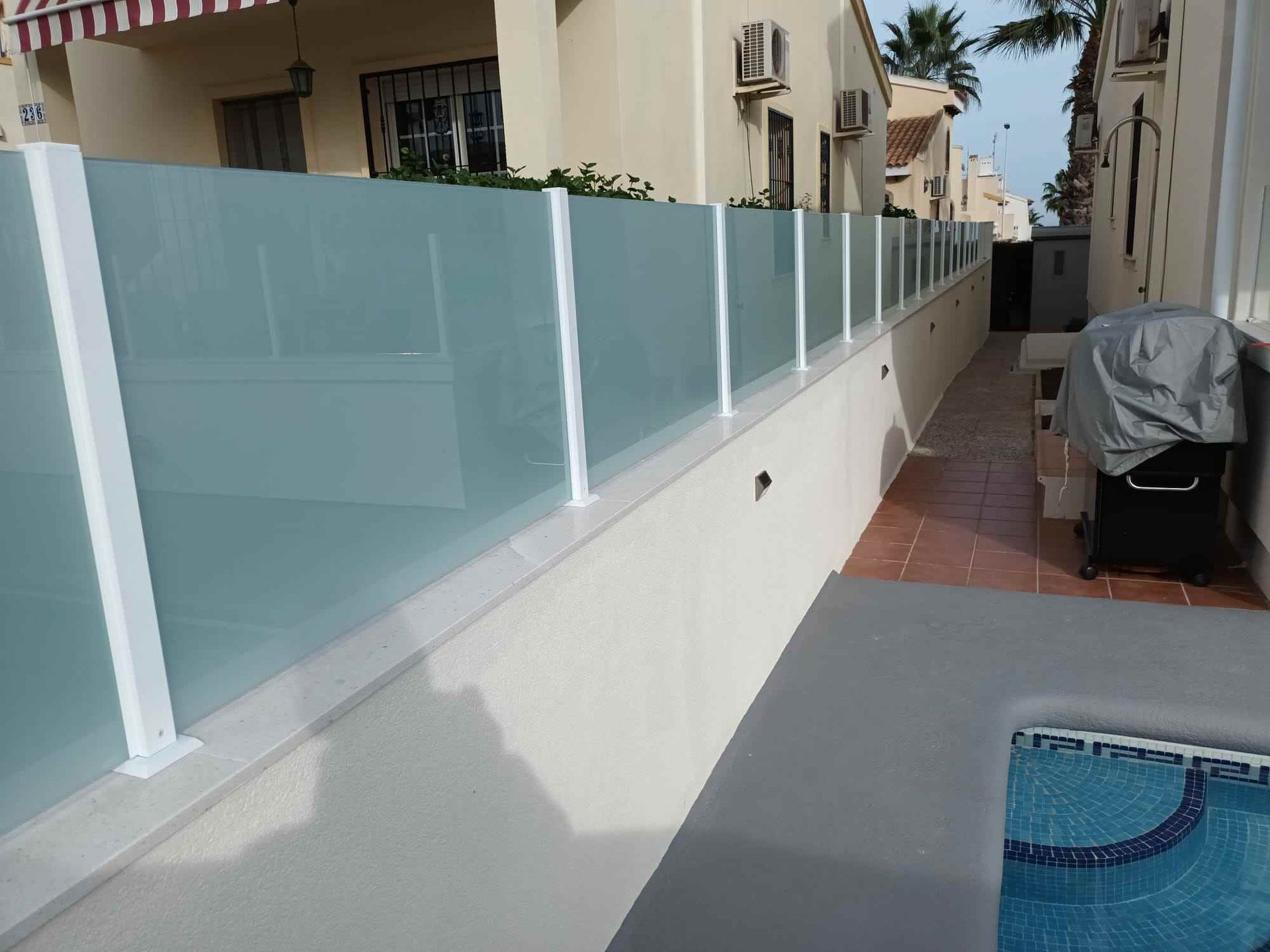 Una valla de cristal rodea una piscina delante de una casa.