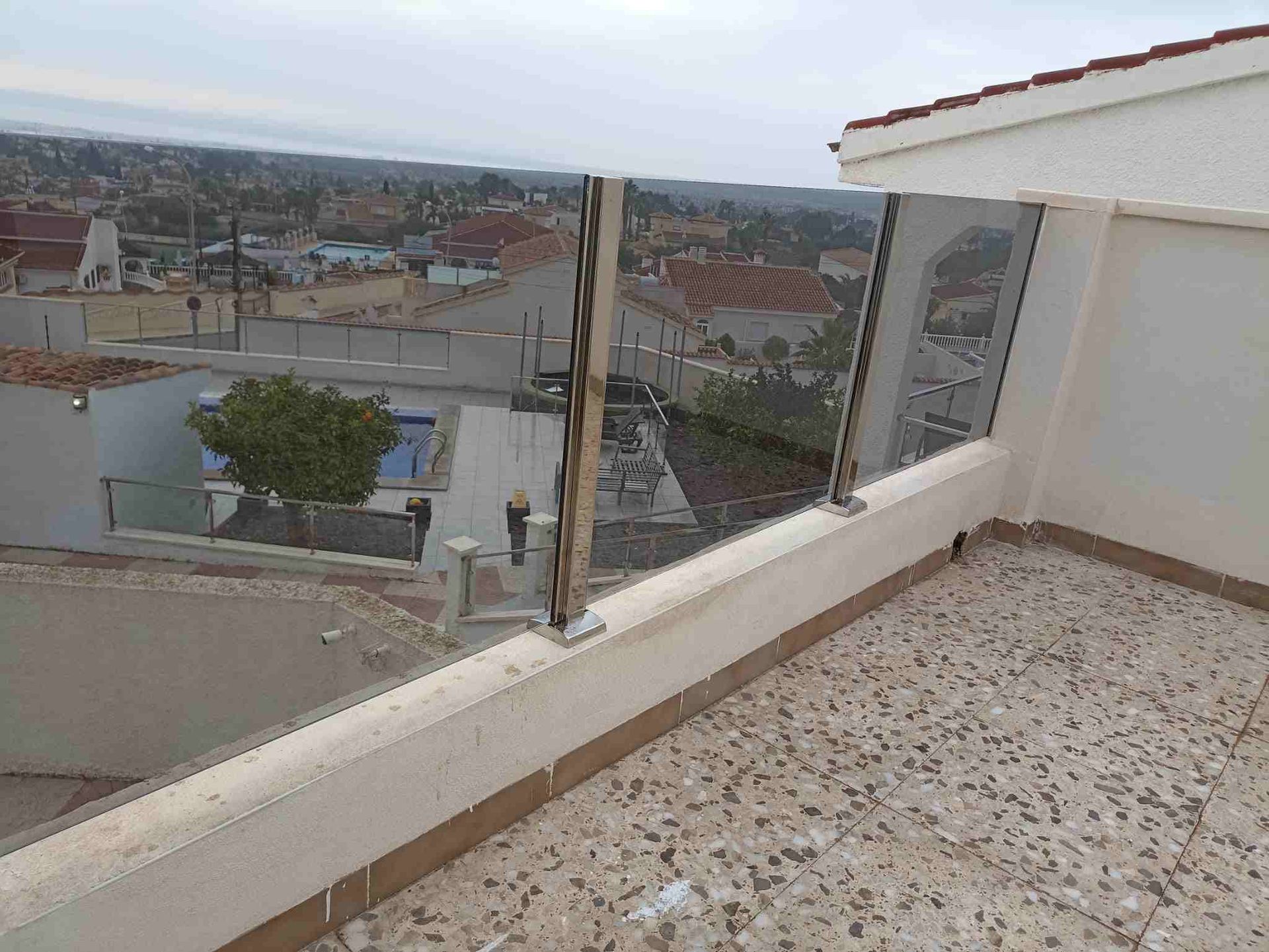 Un balcón con barandilla de cristal y vista a una ciudad.