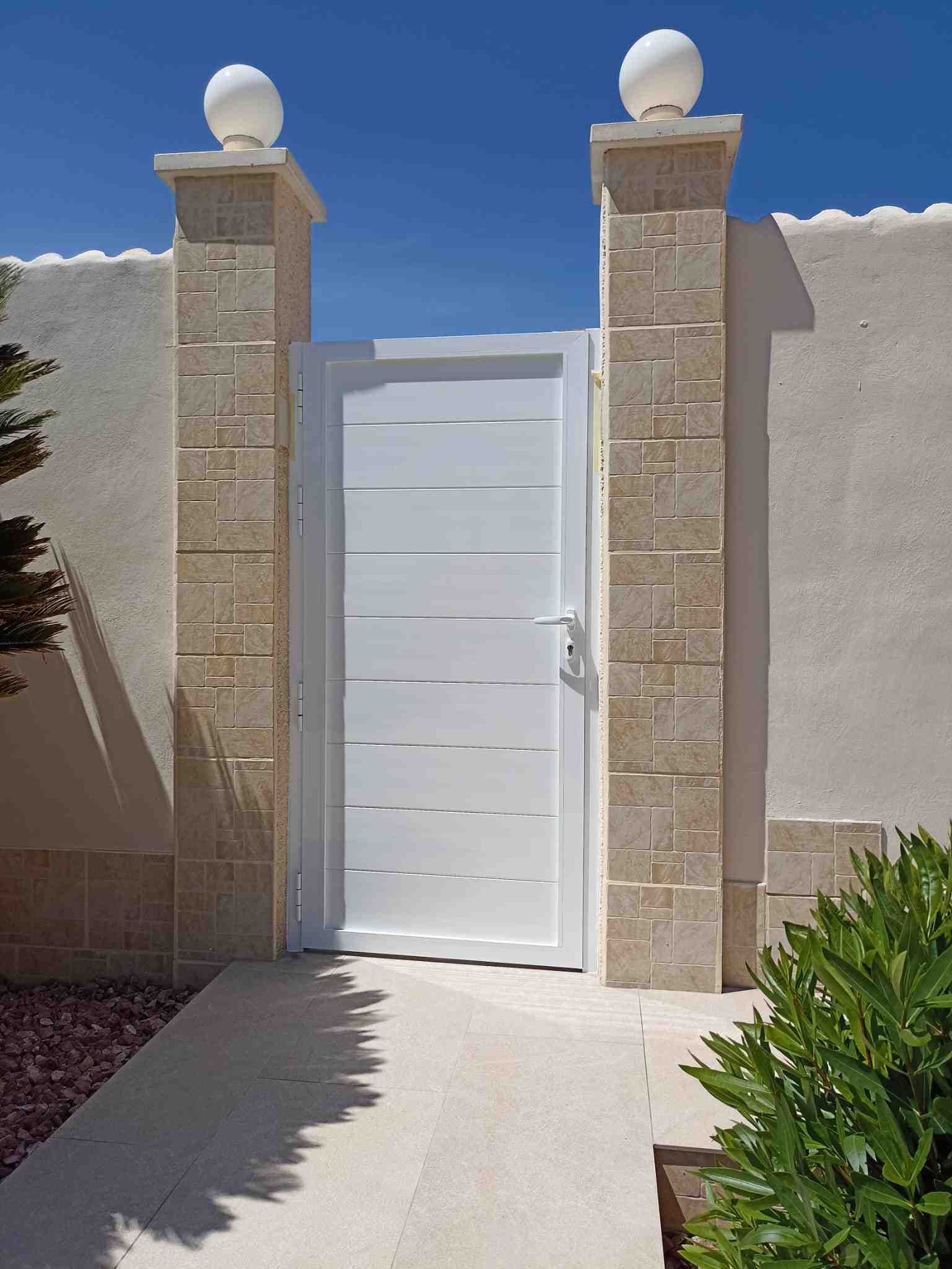 Una puerta blanca está rodeada de pilares de ladrillo y un muro de piedra.