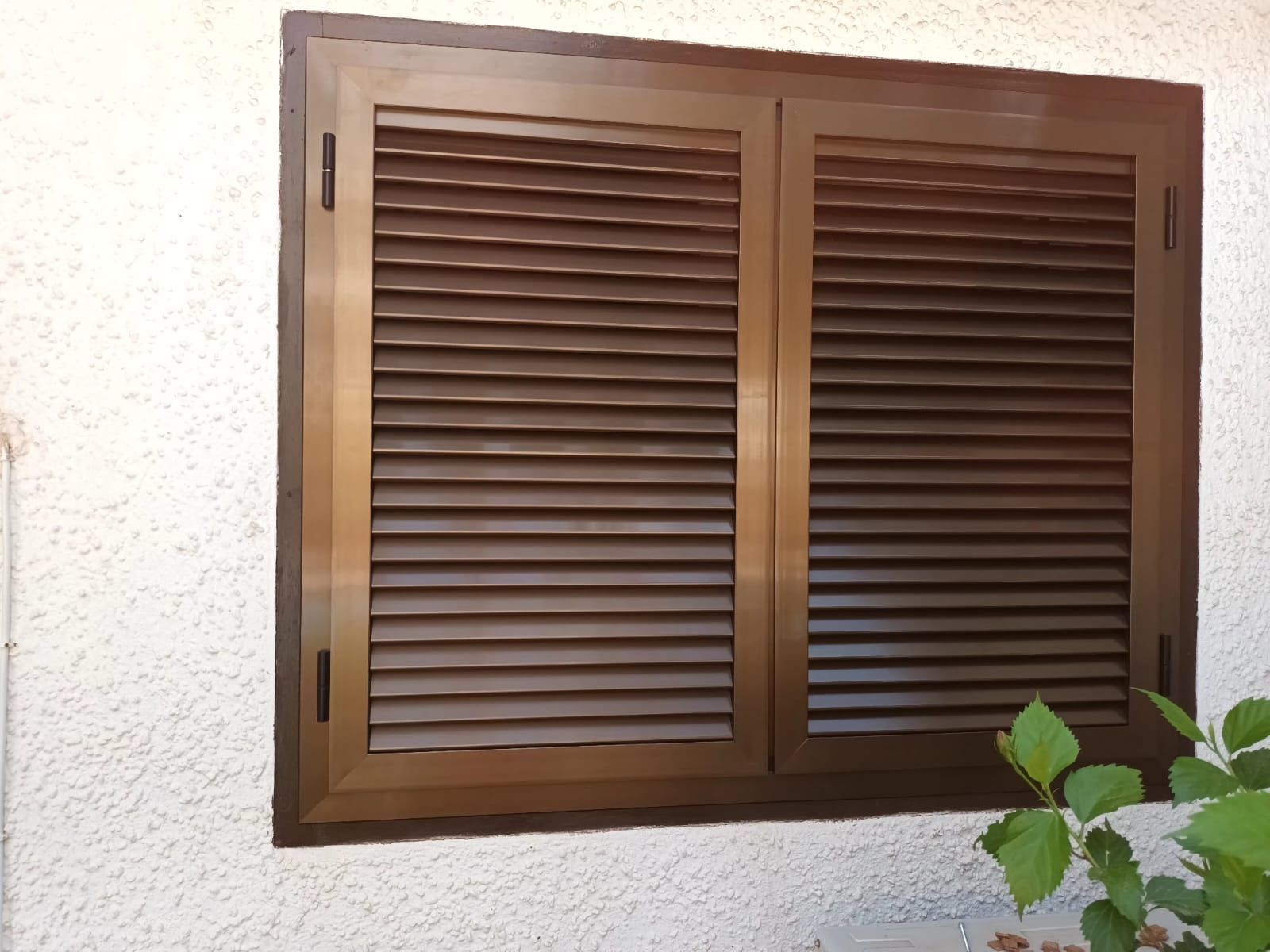 Una ventana con contraventanas marrones en una pared blanca.