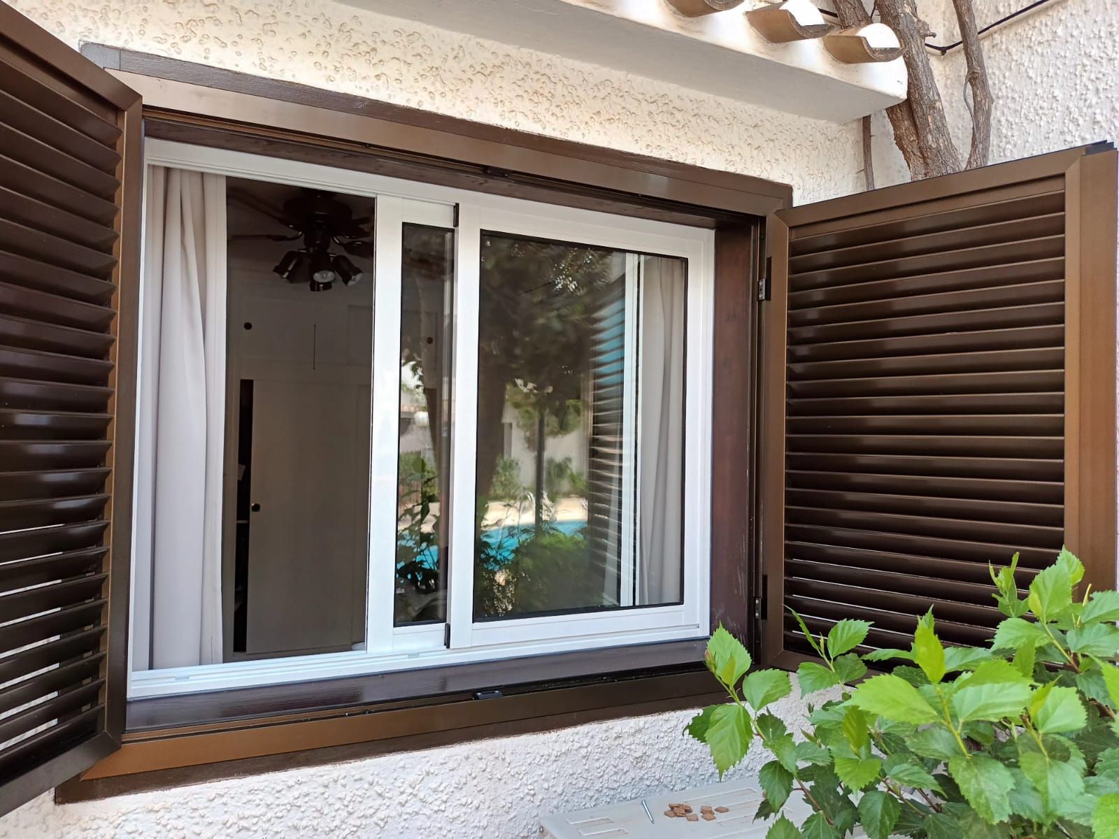 Una gran ventana con contraventanas marrones se abre a un patio.