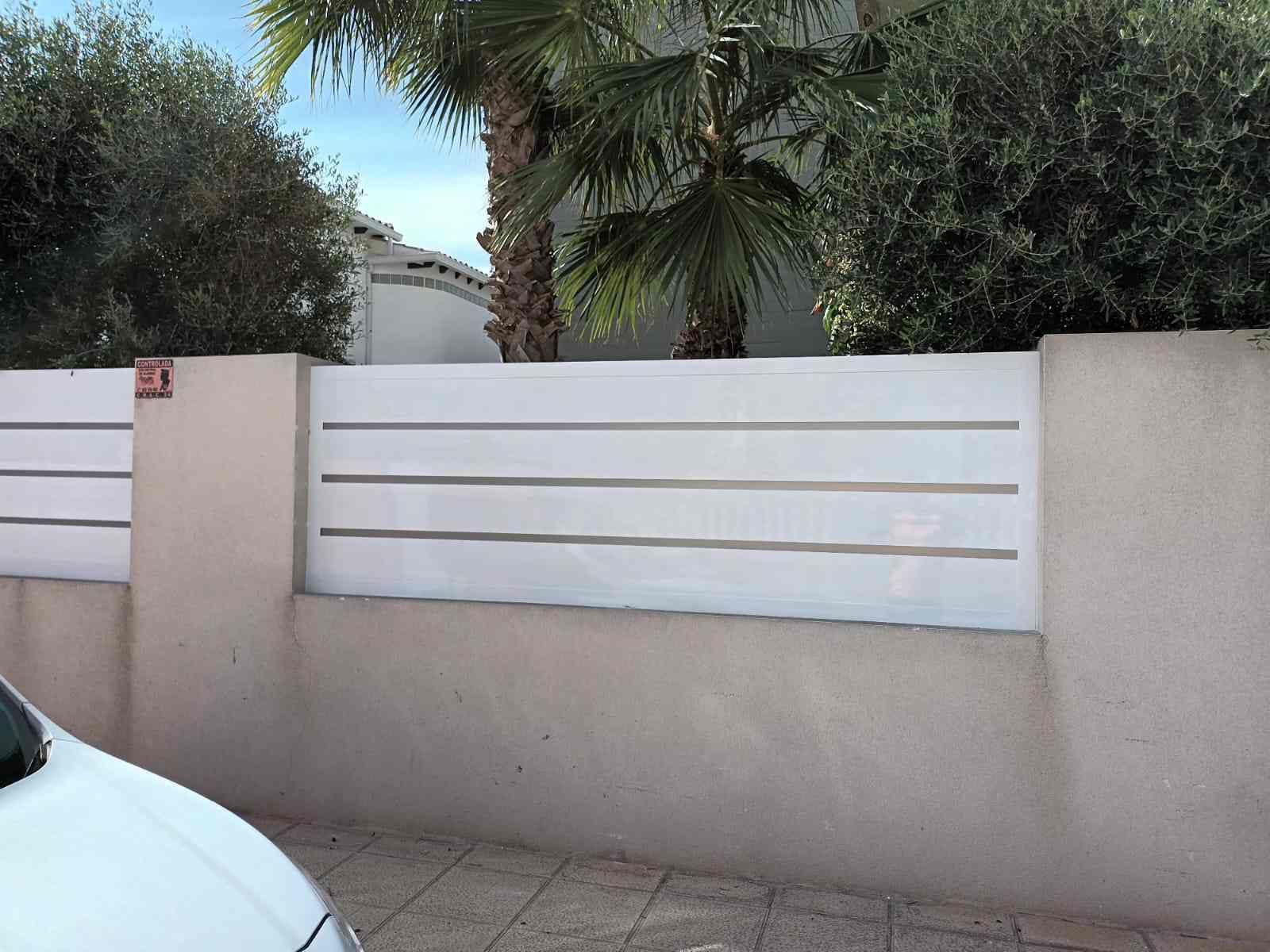 Un coche blanco está aparcado delante de una valla blanca.