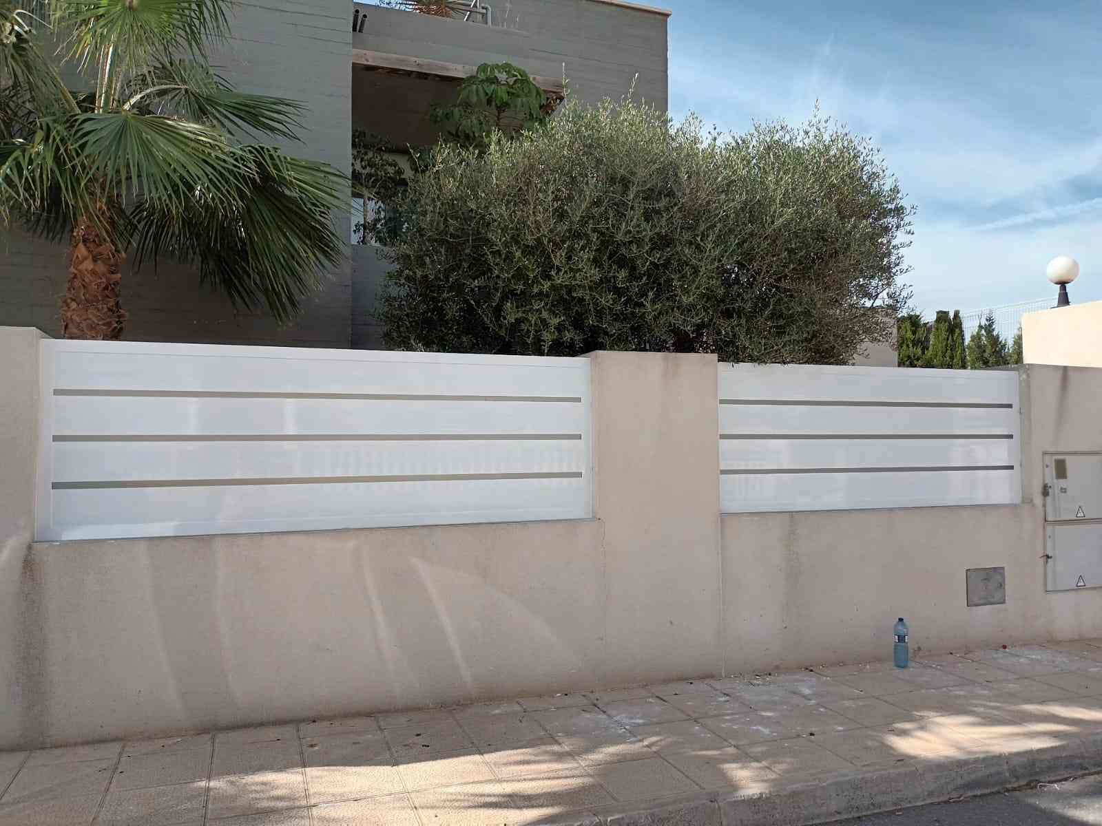 Una valla blanca con una palmera al fondo.