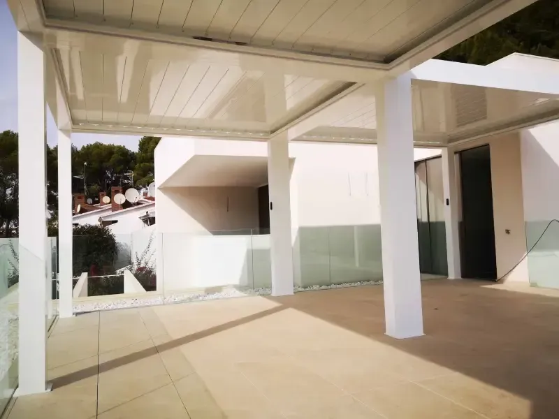 Un balcón con pérgola y barandilla de cristal.