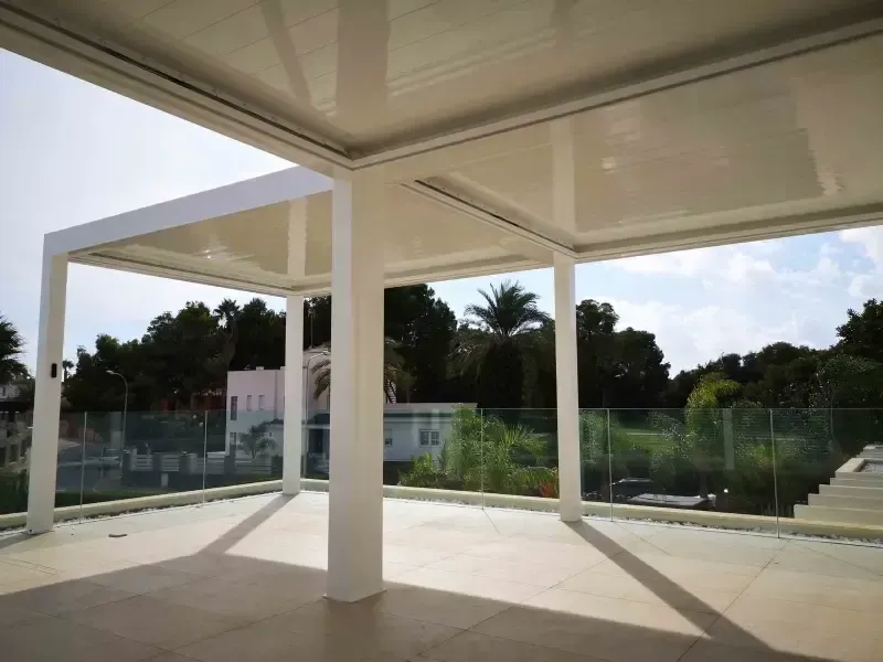 Un balcón vacío con pérgola y barandilla de cristal.