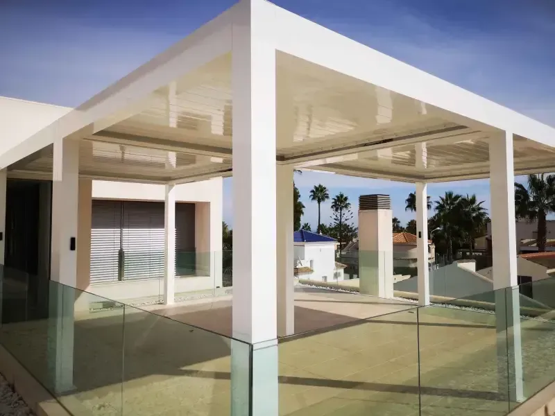 Una pérgola blanca con barandilla de vidrio en el costado de un edificio.