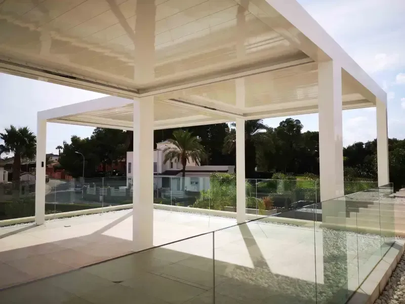 Un balcón con pérgola y barandilla de cristal.
