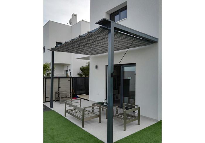 Un patio con pérgola y sillas frente a una casa blanca.