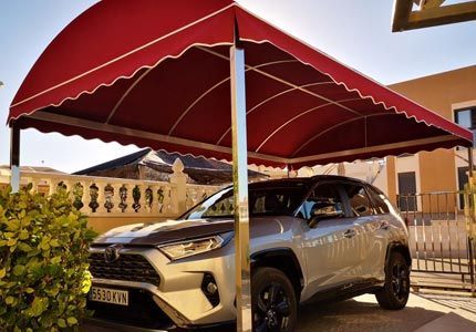 Un coche está aparcado bajo un toldo rojo delante de un edificio.