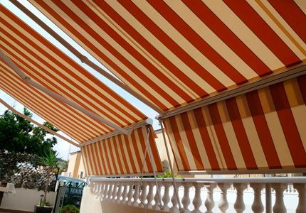 Un toldo de rayas rojas y blancas cubre un balcón.