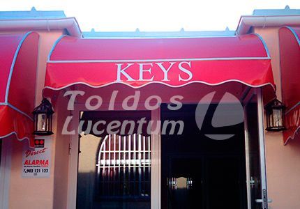 Un toldo rojo sobre una puerta que dice llaves toldos lucenum