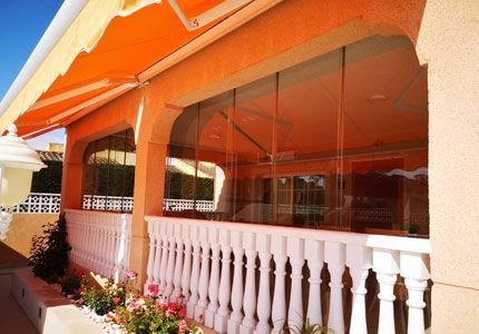 Un balcón con barandilla blanca y toldo naranja.