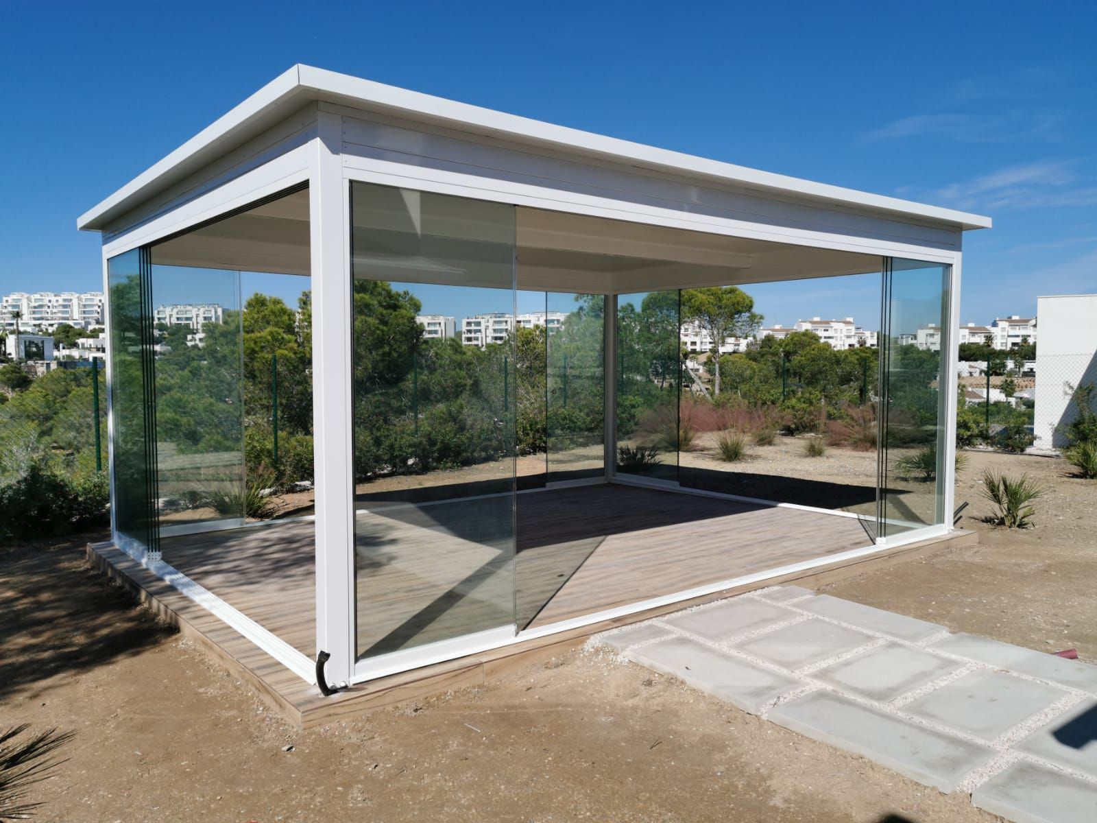 Un mirador blanco con puertas corredizas de vidrio se encuentra en el medio de un campo.