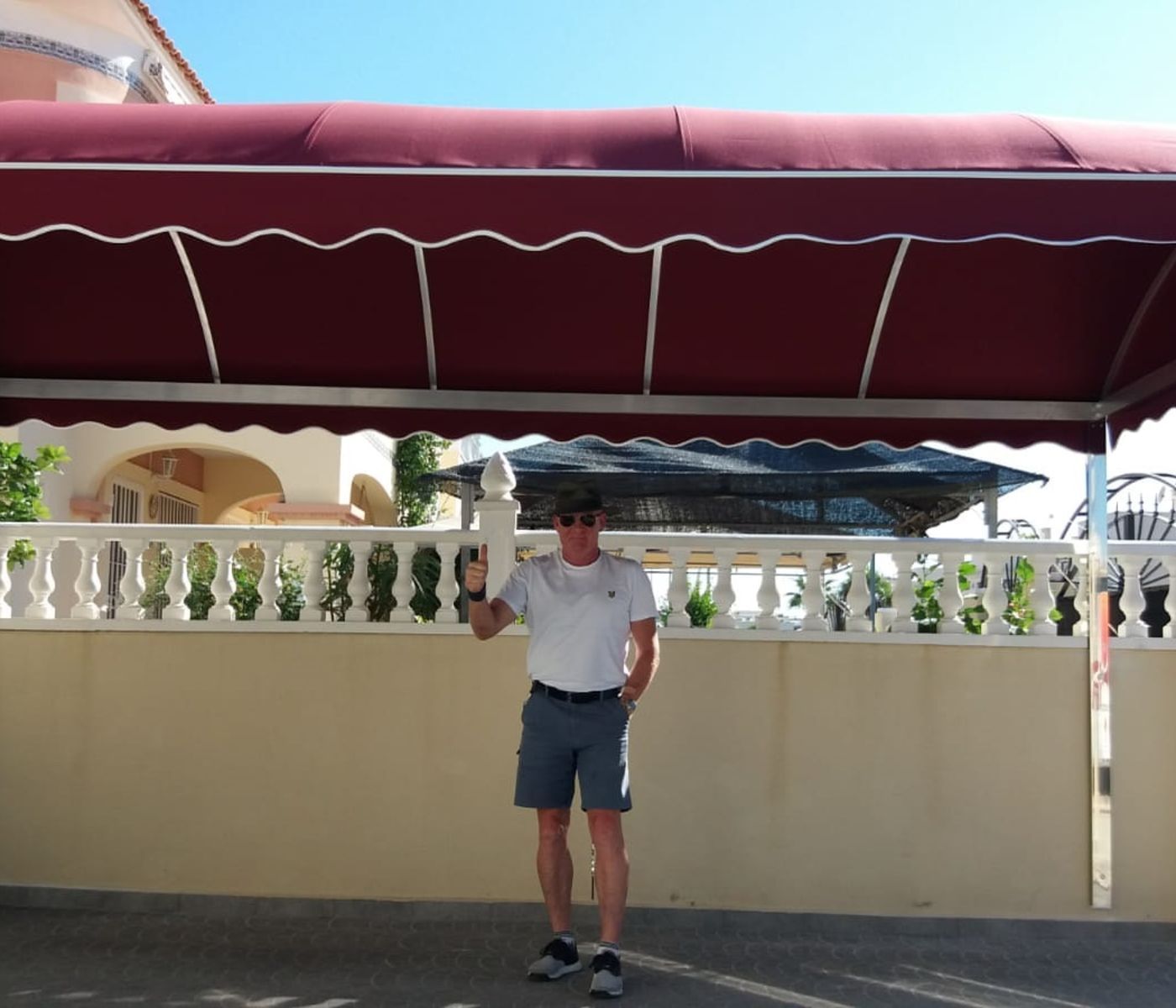 Un hombre con gafas de sol se encuentra bajo un toldo rojo.