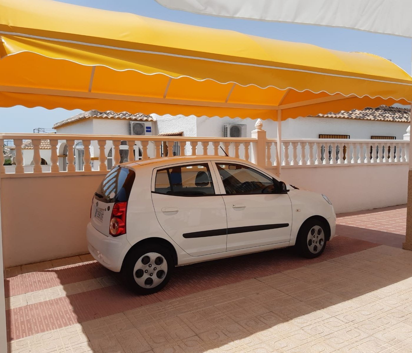 Un coche blanco está aparcado bajo un toldo amarillo.