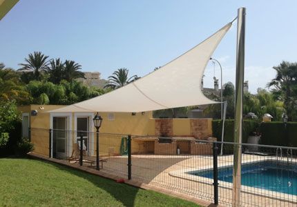 Una vela blanca cubre una piscina frente a una casa.