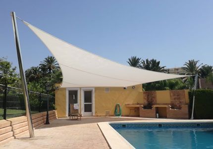 Una vela blanca cubre una piscina frente a una casa.