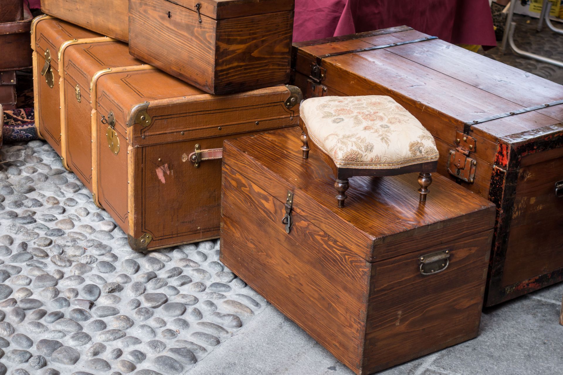 Des malles en bois anciennes empilées dans une rue pavée, avec un petit tabouret sur l'une d'elles.