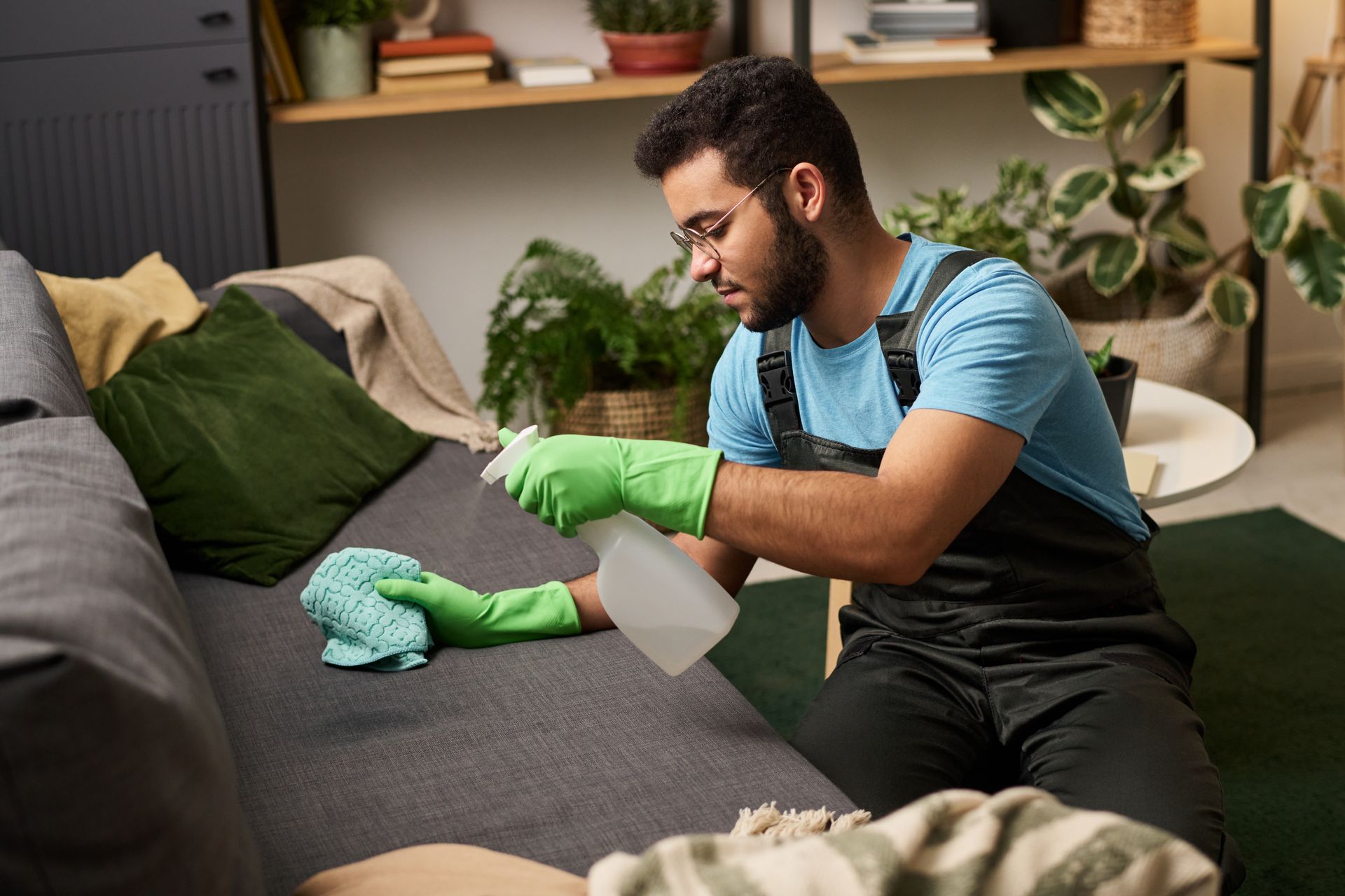 Une personne nettoie un canapé avec des gants verts dans un salon confortable