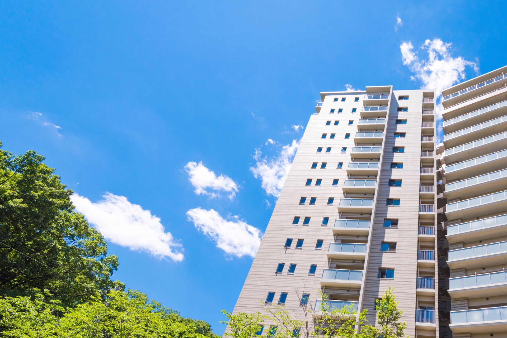 Immeuble d'appartements imposant se détachant sur un ciel bleu éclatant, avec des nuages et des arbres verts en contrebas.