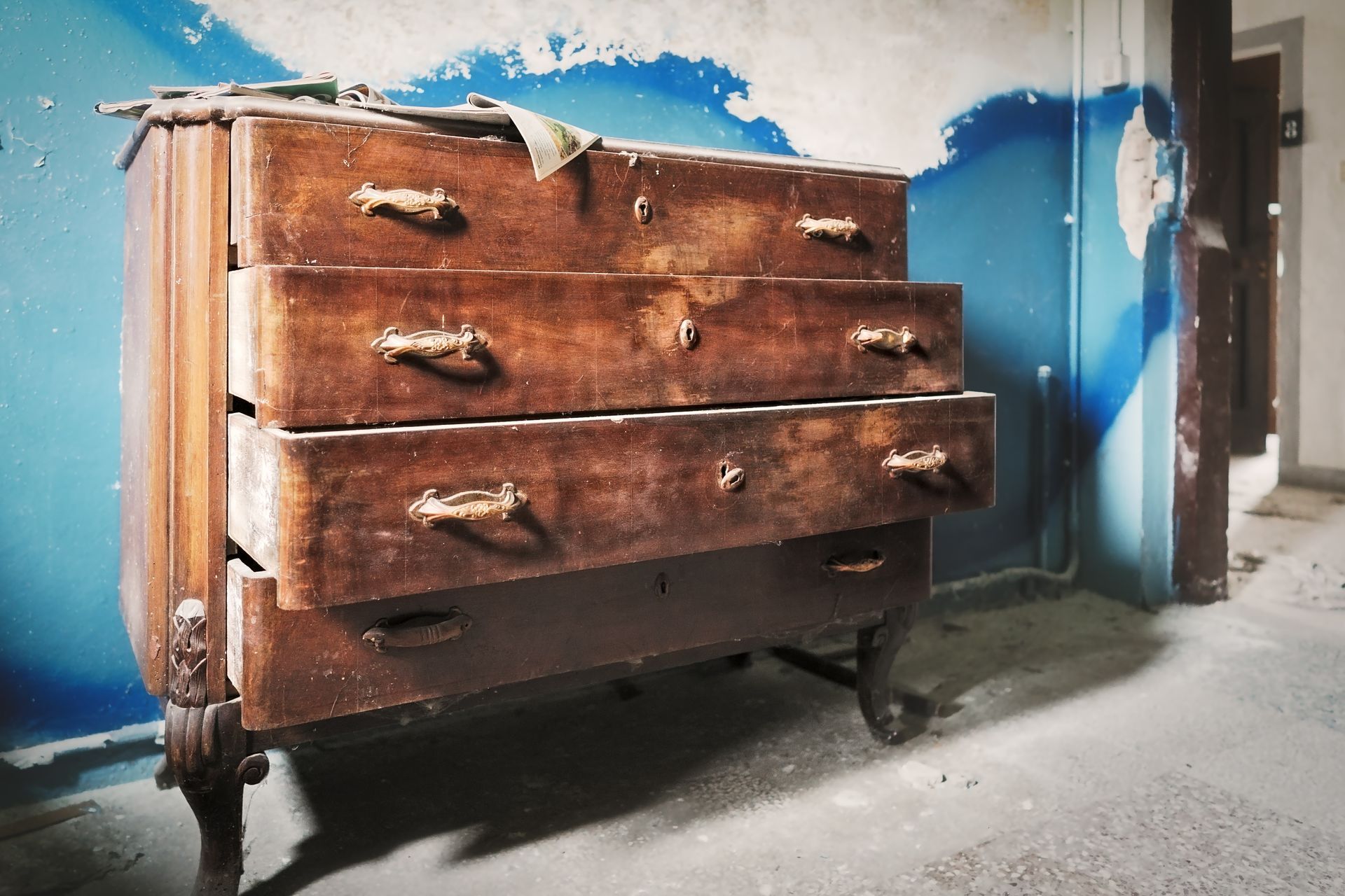 Commode rustique en bois avec tiroirs, placée contre un mur bleu et blanc dans une pièce usée