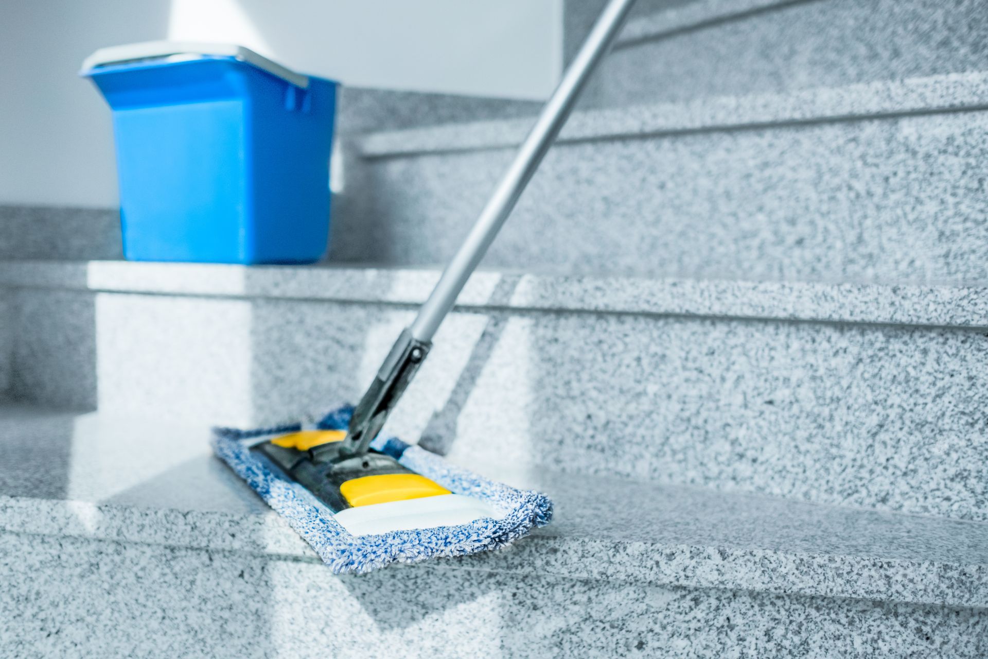 Balai et seau de nettoyage bleu sur un escalier gris.
