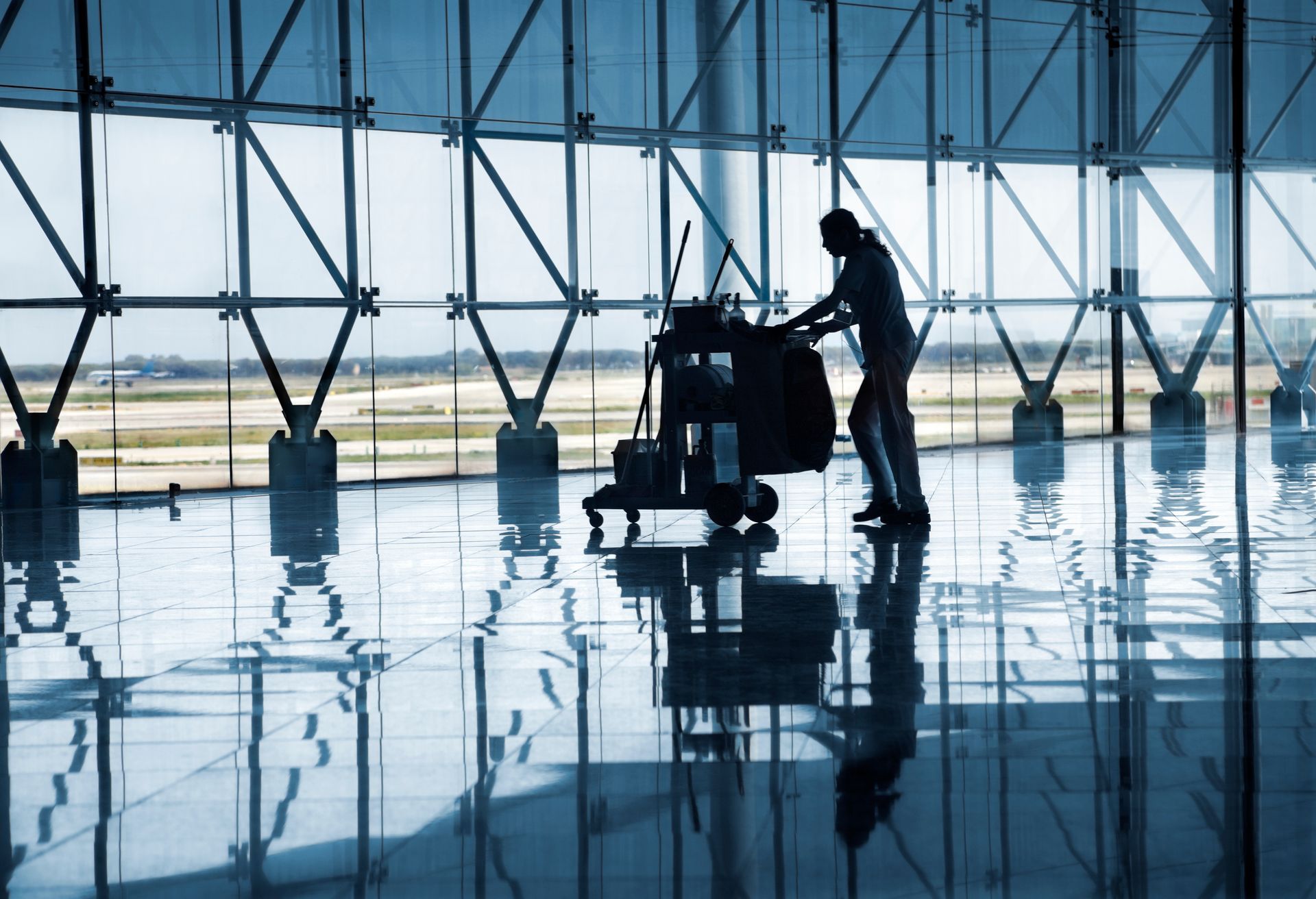 Silhouette d'une personne poussant un chariot à bagages dans un terminal d'aéroport lumineux au sol réfléchissant