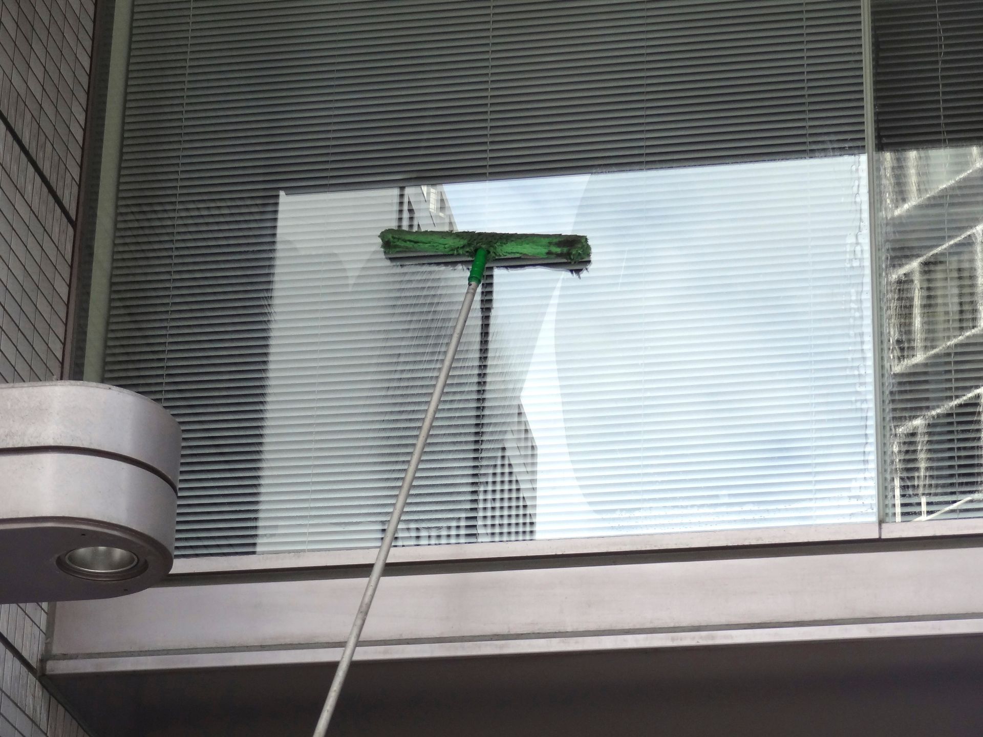 Raclette verte pour le nettoyage des vitres fixée à une longue perche contre la façade vitrée d'un immeuble