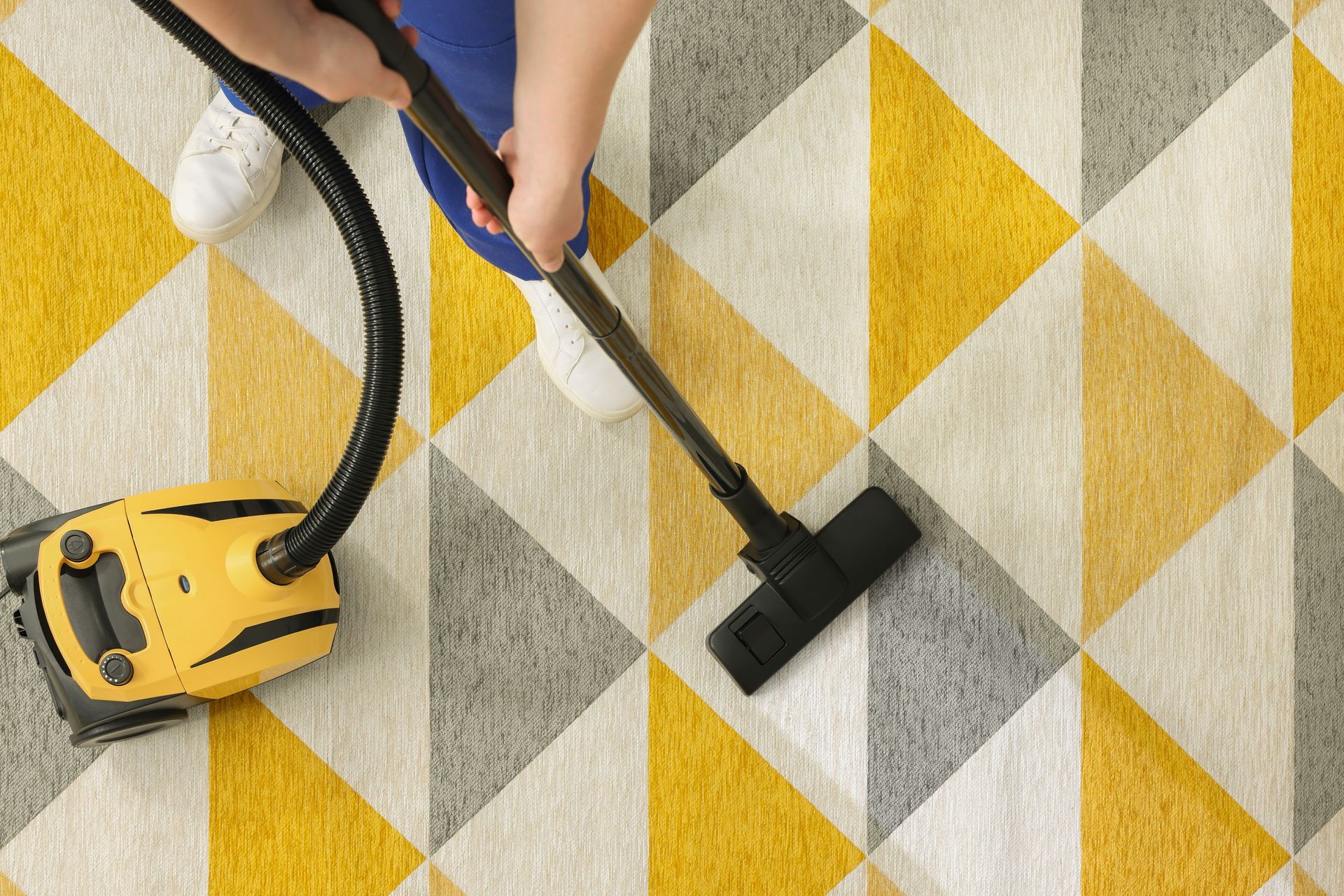 Personne passant l'aspirateur sur un tapis géométrique jaune et gris.