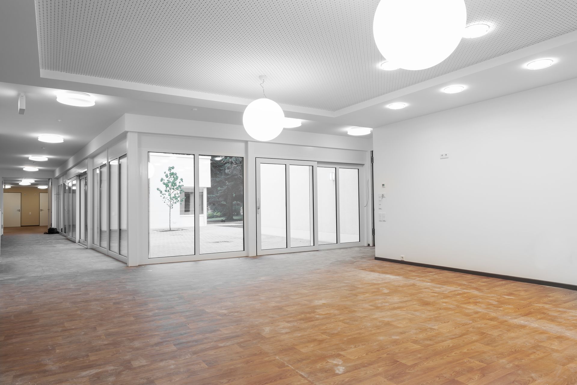 Hall d'entrée vide et lumineux avec portes vitrées, parquet, murs blancs et luminaires ronds au plafond
