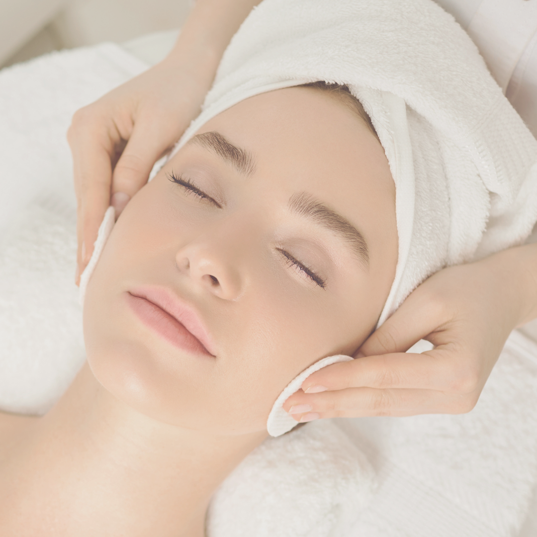 Mujer recibiendo un tratamiento facial en un spa. Una persona le aplica suavemente discos de algodón en la cara, con los ojos cerrados.