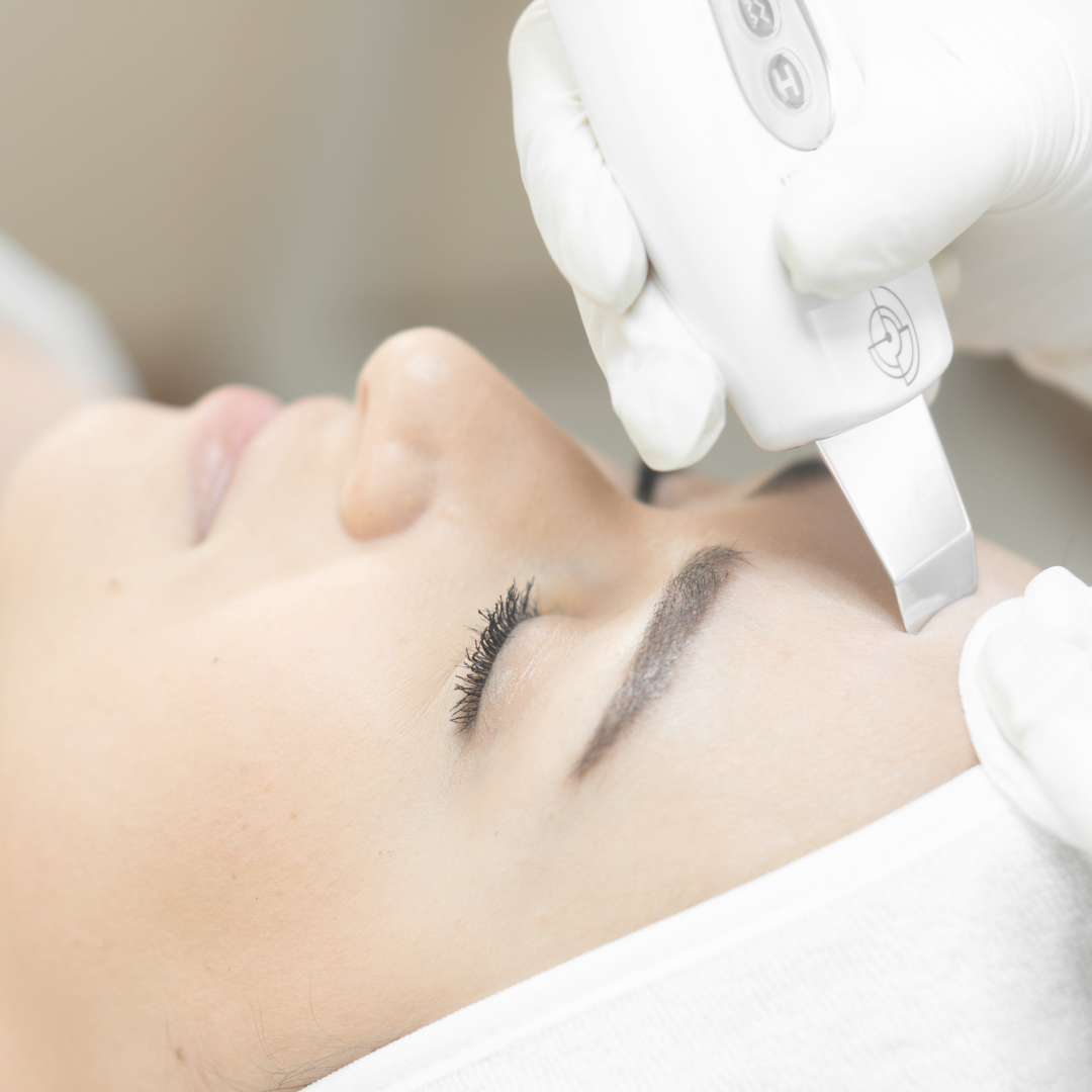 Una persona que recibe un tratamiento facial, con una mano enguantada sosteniendo una herramienta cerca de la frente.