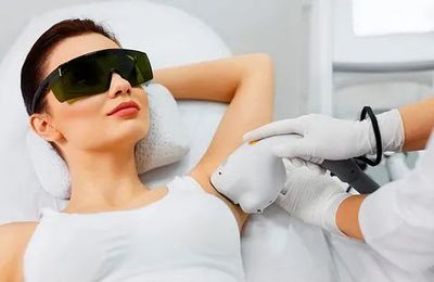 Mujer recibiendo depilación láser en las axilas en una clínica, con gafas protectoras. El médico le está aplicando un dispositivo en la axila.