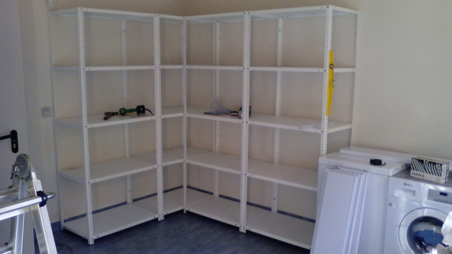 Un lavadero con estantes, una escalera y una lavadora.