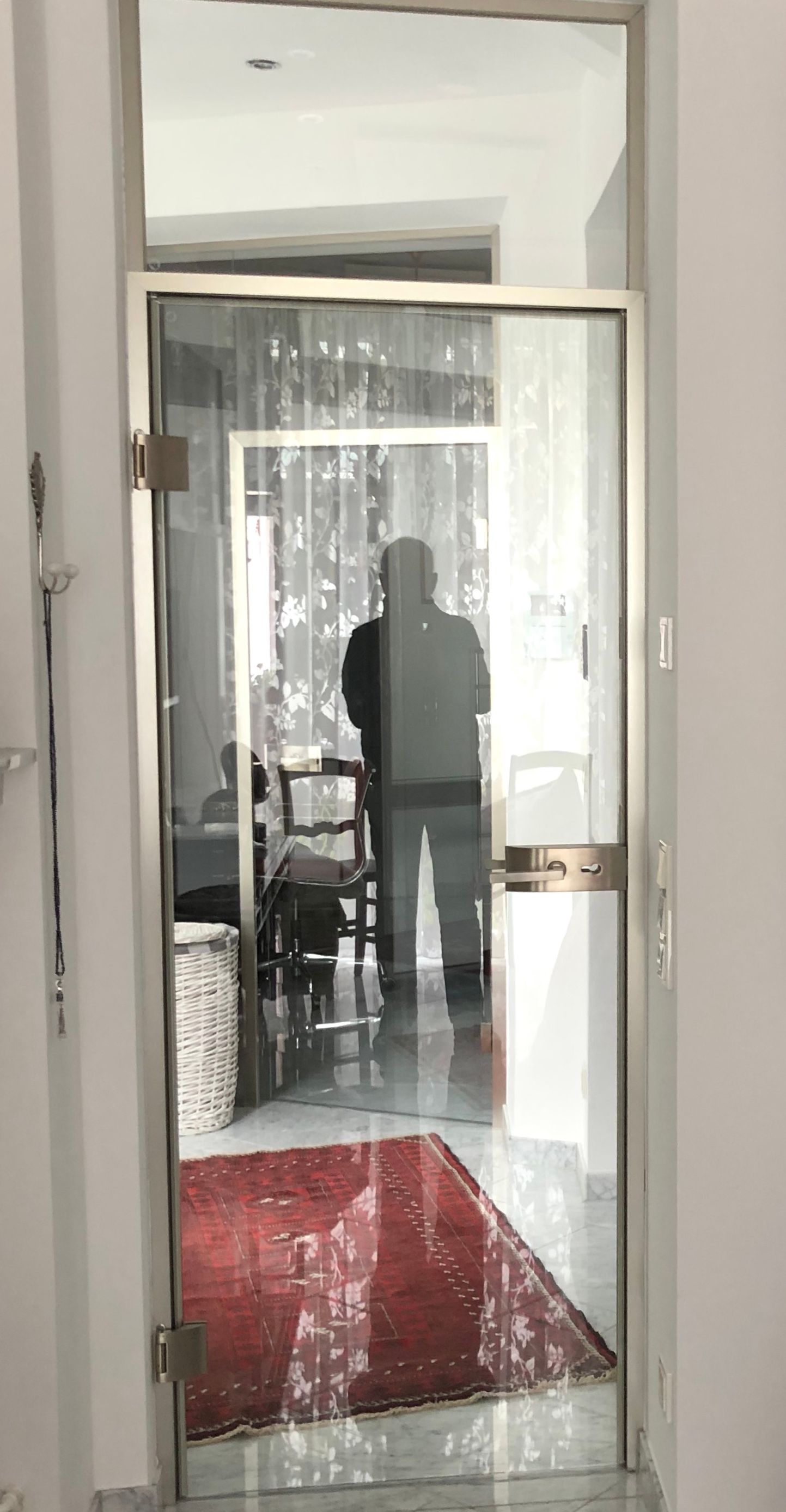 Eine Glastür spiegelt eine Person wider, die in einem Flur steht. In der Spiegelung ist ein roter Teppich zu sehen.