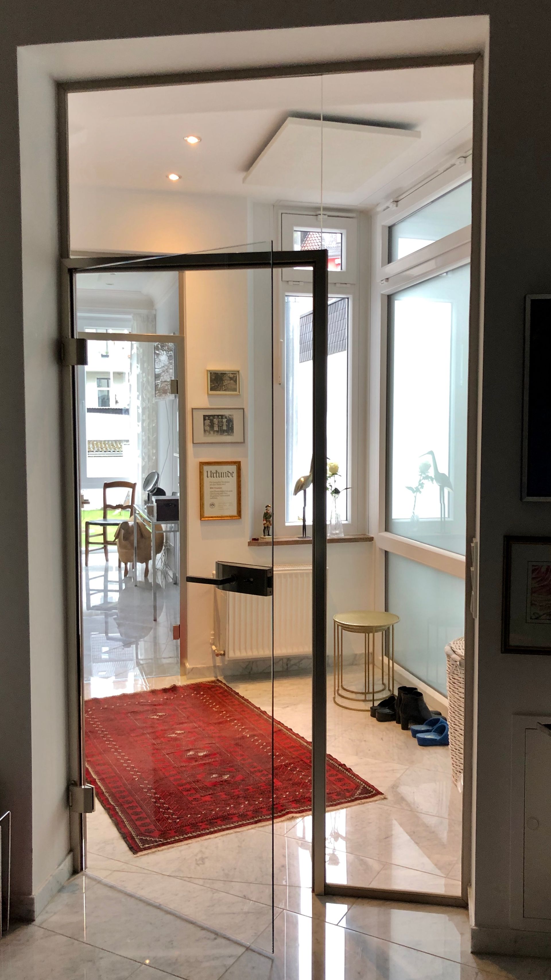 Eine Glastür in einem Haus gibt den Blick auf einen Flur mit einem roten Teppich und Fenstern auf der rechten Seite frei.
