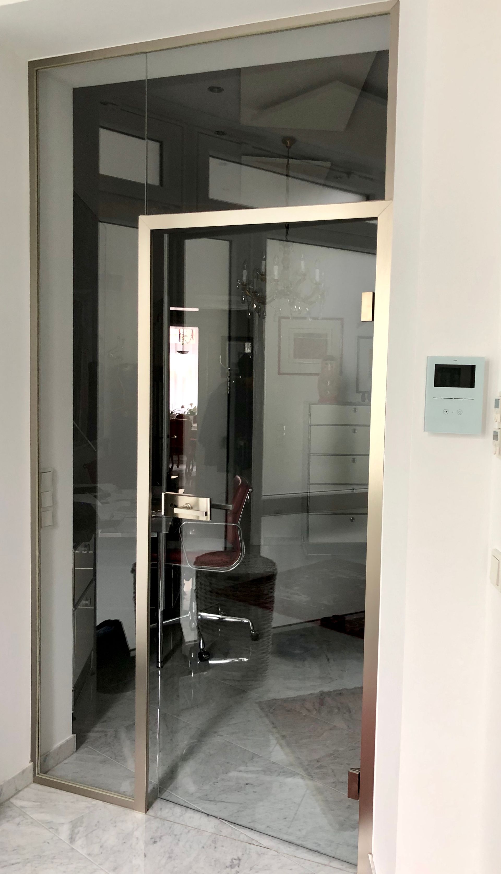 Glastür mit Metallrahmen, die einen Raum mit einem Stuhl und Gegenständen freigibt; Innenraumgestaltung.